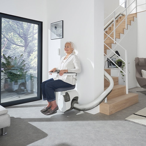 sillas-salvaescaleras-curva mujer mayor subiendo las escaleras en una silla salvaescaleras